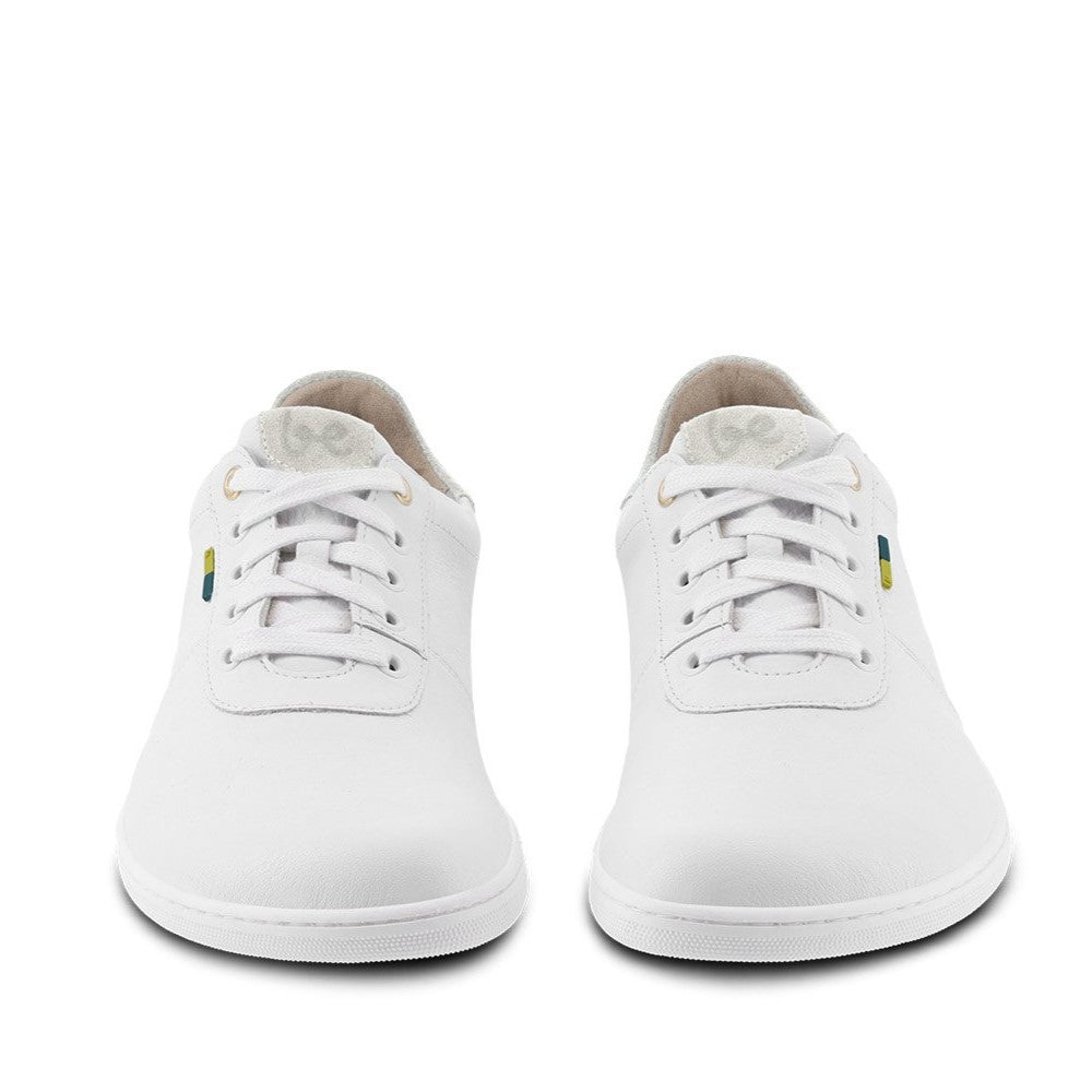 A photo of Be Lenka Royale sneakers made with a leather upper and a rubber sole. The sneakers are a white color and the area around the heel is beige, they have small yellow and blue tag on the side. Both shoes are shown beside each other from the front against a white background. #color_white-beige