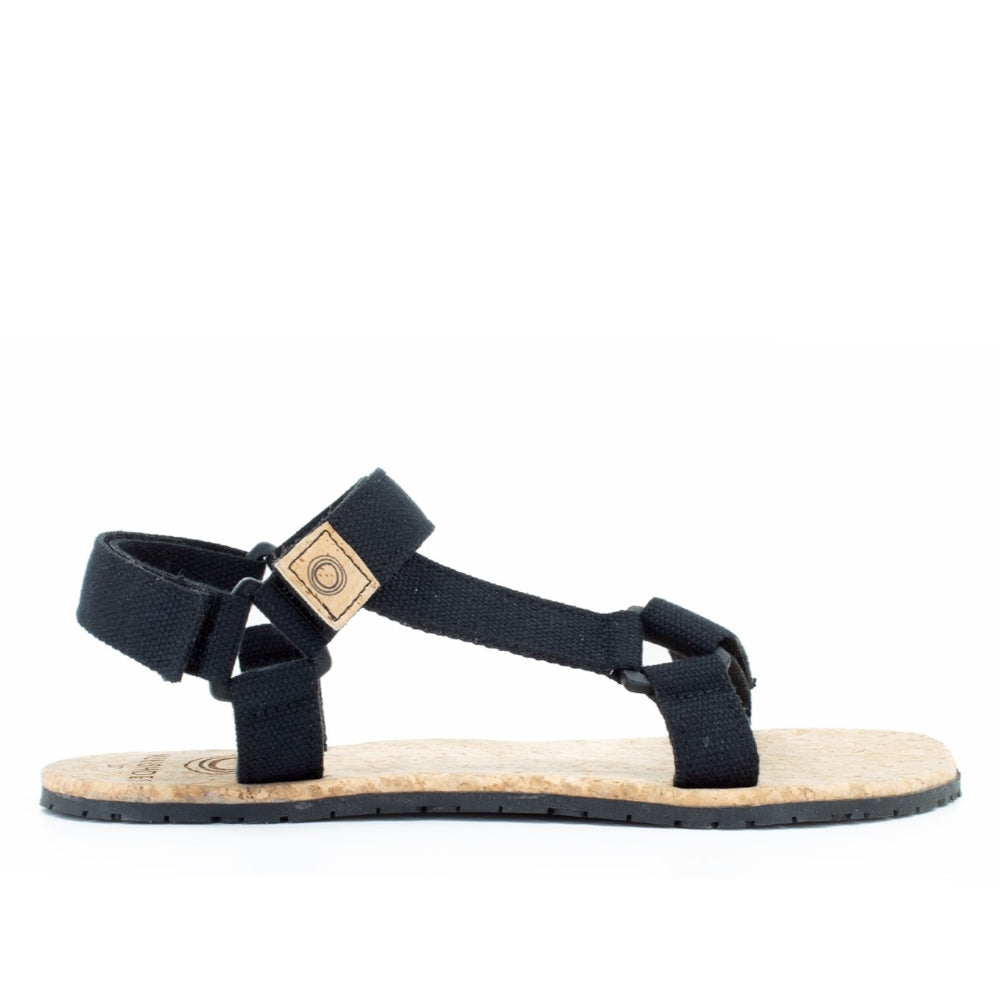 Black Mukishoes Solstice. Sandals have thicker cotton adjustable straps going over the toes and surrounding the ankle with straps connecting the toe and ankle straps. Footbed is quark and sole is a thin black rubber. Right shoe is shown here facing to the right against a white background. #color_black