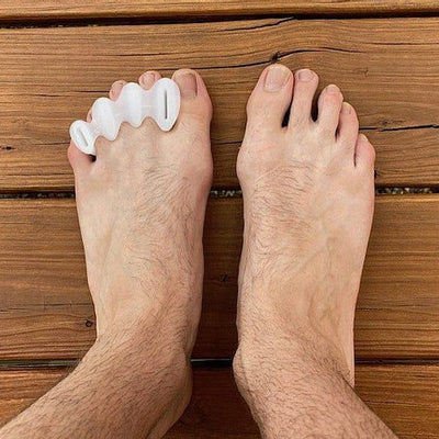 A photo of correct toes clear toe spacers made from silicone. A man’s feet are shown he is standing on a wood porch wearing the correct toes to help with his mild bunions. 