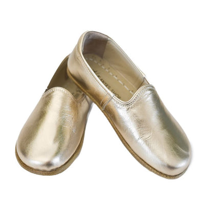 A photo of Gold Yasemin Leather loafers Designed by Anya with a leather upper and tan rubber soles. The loafers have a small curve up on the top of the foot for design. Shoe is shown with the left heel stacked on top of the right shoe opening against a white background. #color_gold