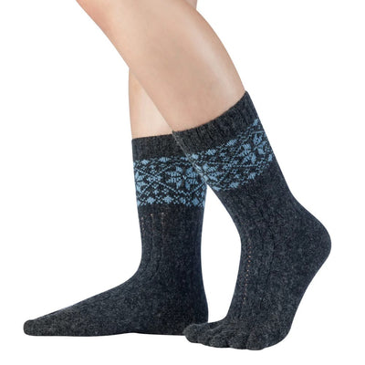 A photo of anthracite and blue knitted toe socks, they have blue detailed snowflake design around the mid-calf. A woman is shown wearing the anthracite/blue colored socks from the mid calf down against a white background. #color_anthracite-light-blue