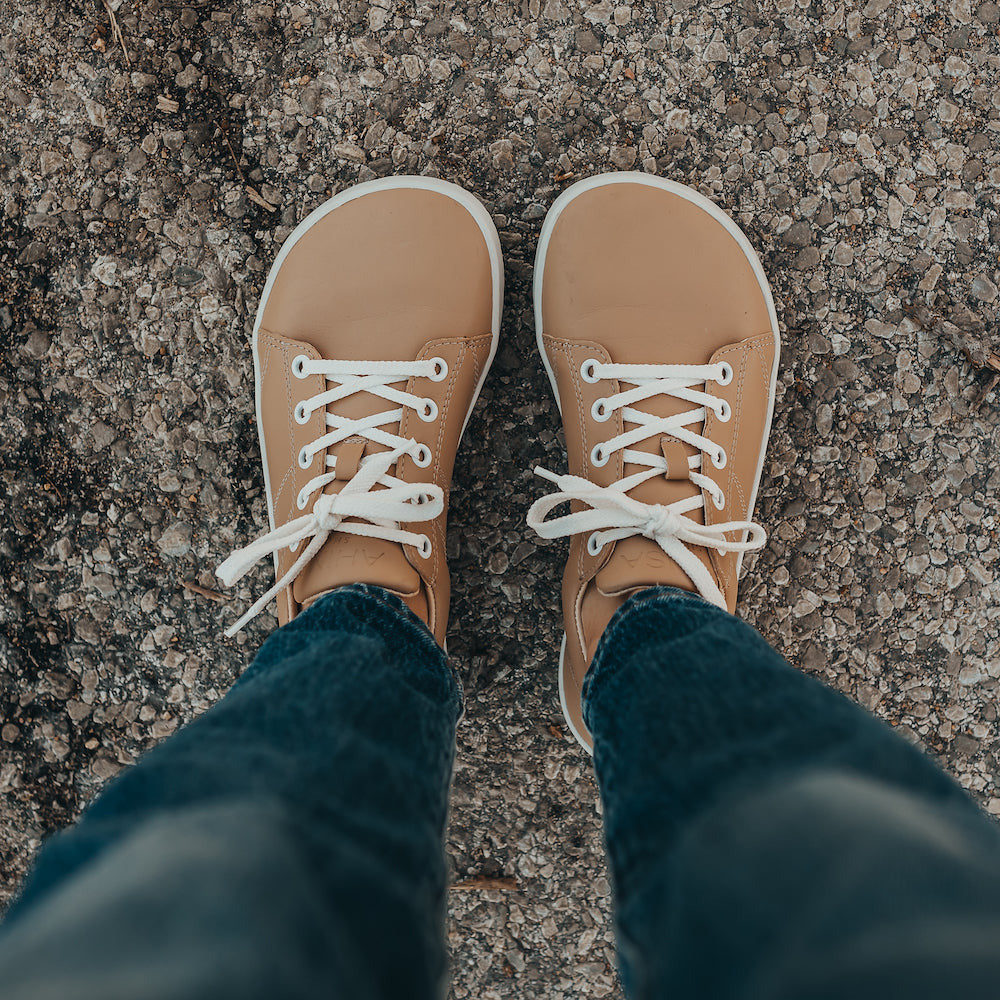 Beige colored vegan sneakers shown on a model. Feet only, top down view of both feet standing on cement. Featuring white laces and a white sole. #color_beige