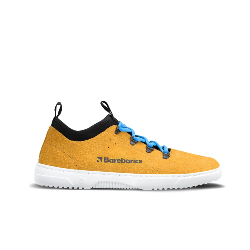 Photo 1 - A photo Barebarics Bronx chunky leather sneaker in yellow with while soles and blue laces. Shoes are surrounded by suede with a black pull-on style tongue and ankle opening. Laces are attached by metal boot eyelets. Right shoe is shown from the right side against a white background. Photo 2 - Both shoes are shown from the top down against a white background. #color_mustard
