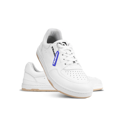 A photo of all white Barebarics Wave classic leath sneakers. Toe box is perforated, the sole is white with tan thread, barebarics brand name is written on the side. Both sneakers are shown, the right sneaker is shown in front of the left sneaker with its heel resting on top of the left sneaker against a white background. #color_all-white