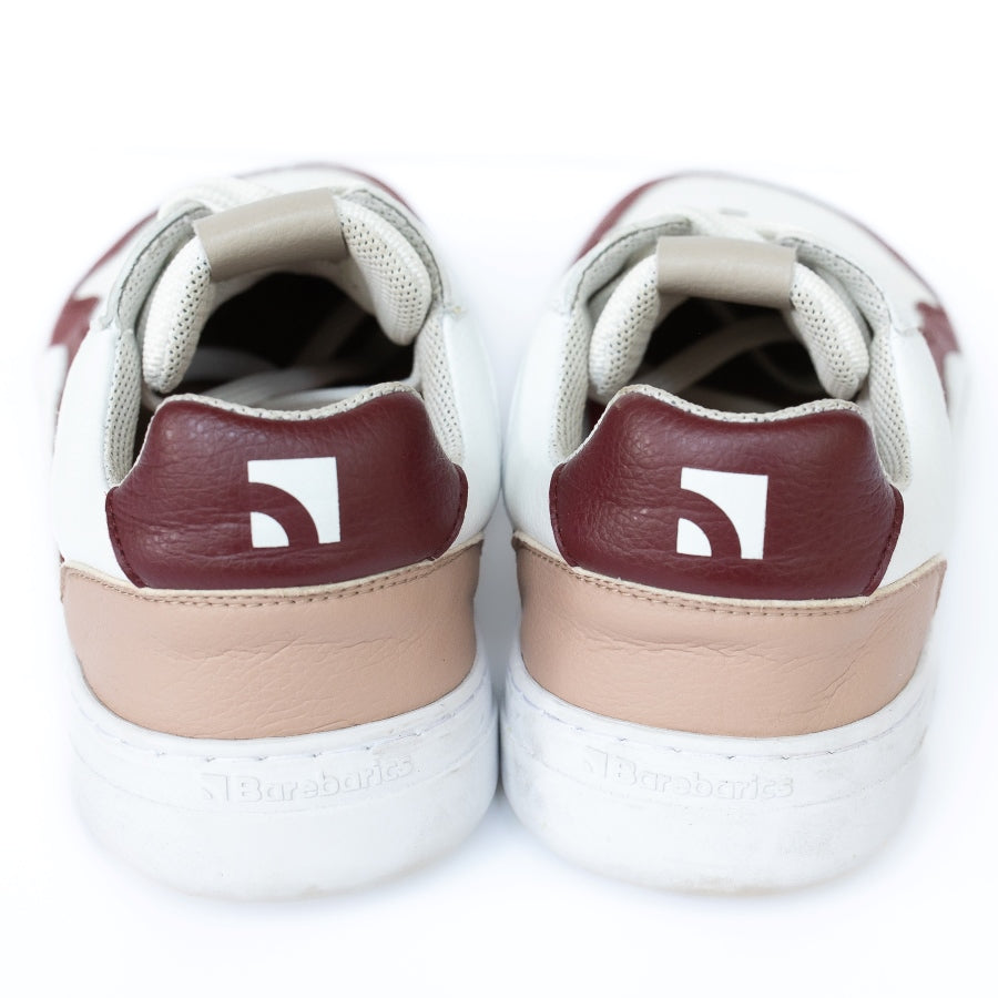Barebarics Zing sneakers made with a leather upper and a rubber sole. The sneakers are white with burgundy accents around the front and side, and a tan accent over the heel. There are perforated spots on the top of the toe box and barebarics branding on the tongue and side. Both sneakers are shown side by side from behind, on a white background. #color_burgundy