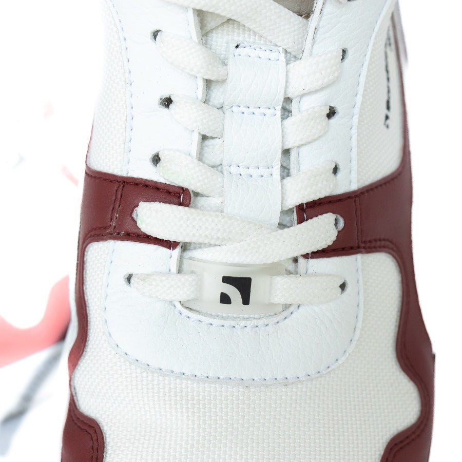 Barebarics Zing sneakers made with a leather upper and a rubber sole. The sneakers are white with burgundy accents around the front and side, and a tan accent over the heel. There are perforated spots on the top of the toe box and barebarics branding on the tongue and side. The left sneaker is shown from above with a close up of the laces, on a white background. #color_burgundy-anya-exclusive