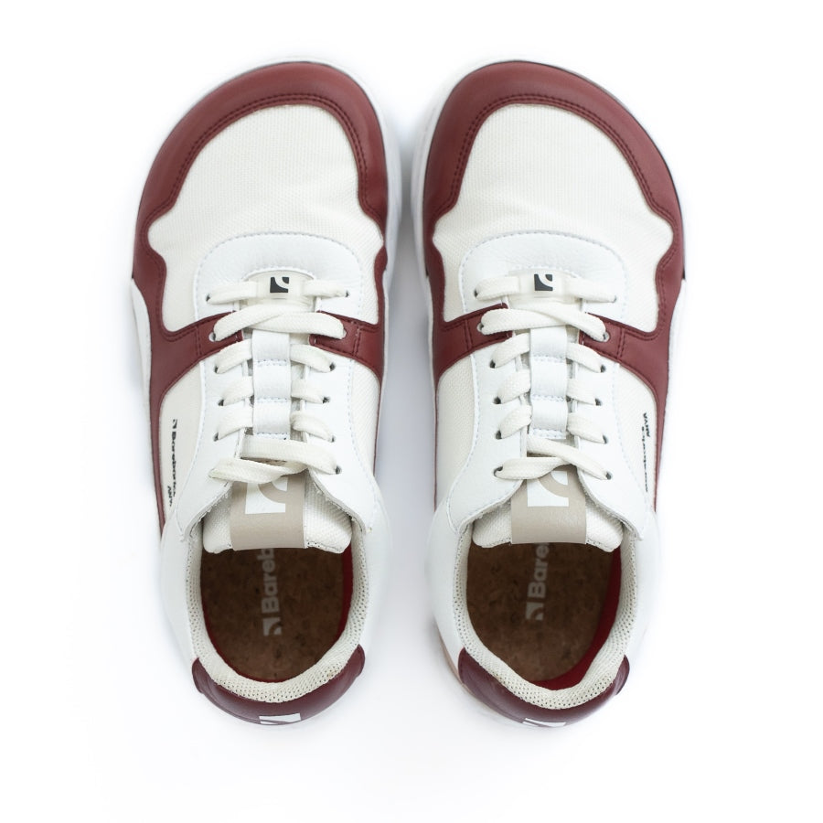 Barebarics Zing sneakers made with a leather upper and a rubber sole. The sneakers are white with burgundy accents around the front and side, and a tan accent over the heel. There are perforated spots on the top of the toe box and barebarics branding on the tongue and side. Both sneakers are shown side by side from above, on a white background. #color_burgundy