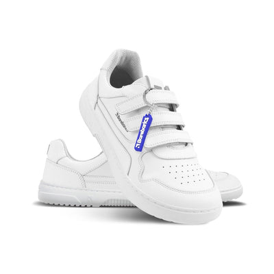 Photo 1 - A photo of white Barebarics Zing leather sneakers. Shoes have perforated spots on the top of the toe box, have barebarics branding on the tongue and side, and a velcro straps instead of laces. Left sneaker is shown facing right with the right shoe heel leaning on the left shoe against a white background. Photo 2 - Both shoes are shown from above against a white background. #color_all-white