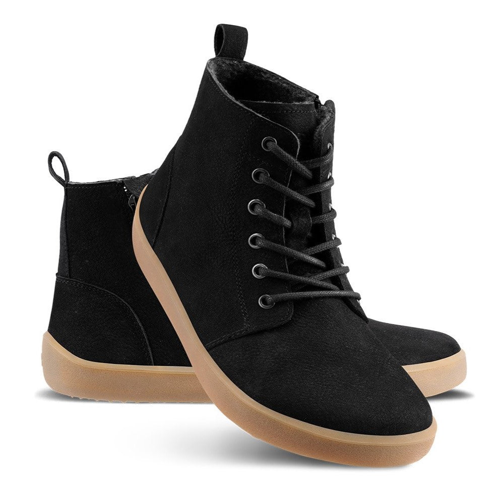 A photo of Be Lenka Atlas ankle zip up boots made from nubuck leather and rubber soles. The boots are black in color with black laces, zippers, a pull tab in the back, and lined with felt. Left boot shown from the left side with the right boot's heel resting diagonally on the left against a white background. #color_matte-black