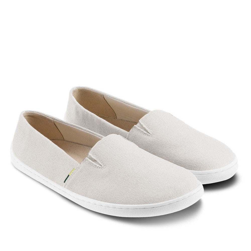 A photo of the Be Lenka Bali canvas slip on, the slip ons are a beige color with a yellow and green tag on the side. Both shoes are shown beside each other facing slightly towards the right against a white background. #color_beige