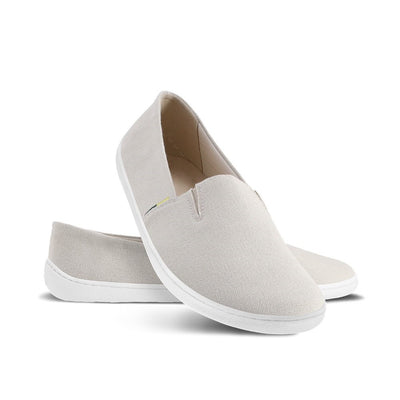 A photo of the Be Lenka Bali canvas slip on, the slip ons are a beige color with a yellow and green tag on the side. Both shoes are shown with the right leaning the heel against the left shoe which is positioned behind it shown on a white background. #color_beige
