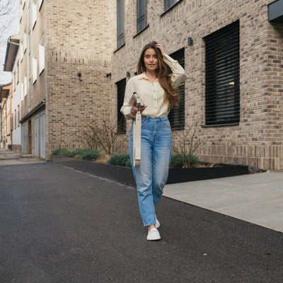 Photo 1 - A photo of Be Lenka Buena penny loafer in all white. The left loafer is shown from the side facing towards the right with the right shoe heel leaning against it against a white background. Photo 2 - Both shoes are shown from the front on feet against a brick housing complex background. #color_all-white