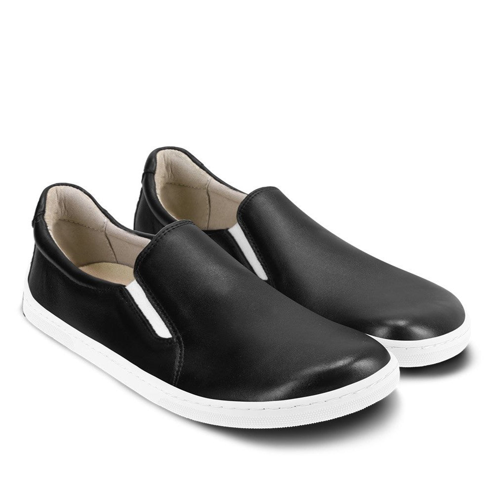 A photo of a black leather slip-on sneaker with white elastic on the sides, and a white sole. Both loafers are shown beside each other angled to the right against a white background. #color_black-white-leather