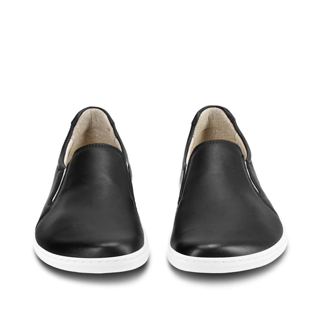 A photo of a black leather slip-on sneaker with white elastic on the sides, and a white sole. Both sneakers are shown beside each other from the front against a white background. #color_black-white-leather