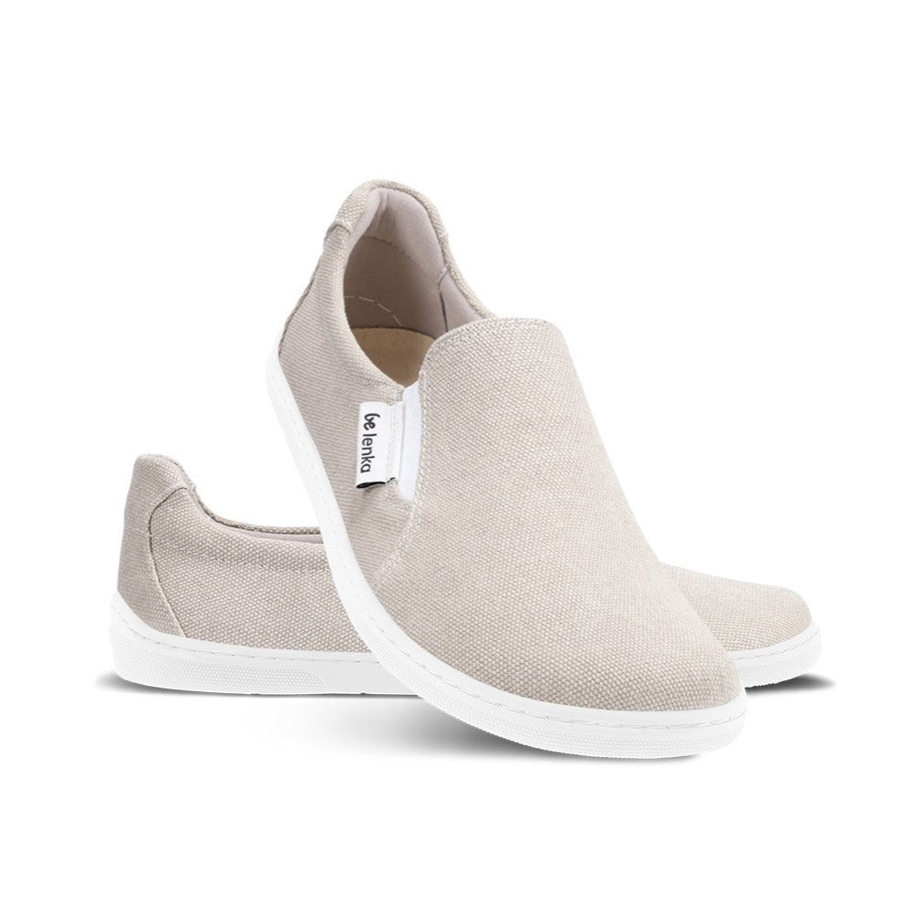 A photo of a sand canvas slip-on sneaker with white elastic on the sides, and a white sole. Both sneakers are shown the right sneaker is shown from the front while resting its heel on the left sneaker behind it against a white background. #color_sand-canvas