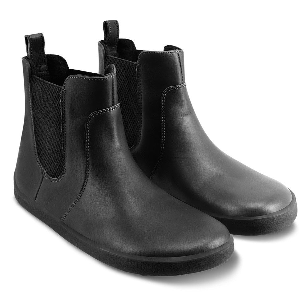 A photo of Belenka Entice Neo boots made from smooth leather and black rubber soles. The boots are black in color with elastic panels on the sides and pull on loops. Both shoes are shown beside each other from the front angled slightly to the right against a white background. #color_black