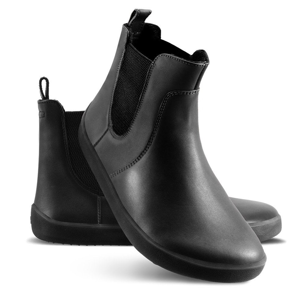 A photo of Belenka Entice Neo boots made from smooth leather and black rubber soles. The boots are black in color with elastic panels on the sides and pull on loops. Both shoes are shown the left shoe is sitting behind the right shoe, the right shoes heel is leaning on the left shoe and is facing downward against a white background. #color_black
