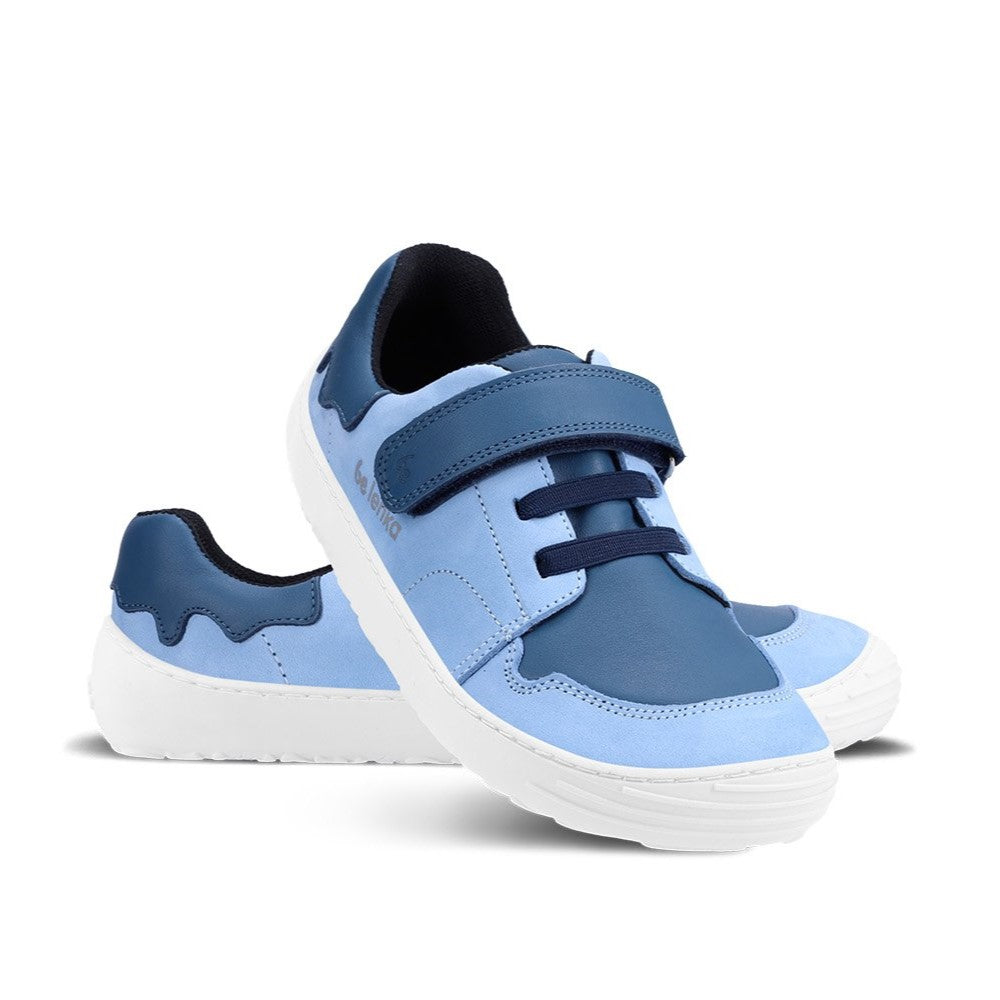 A photo of blue Be Lenka Gelato kids leather sneakers with white rubber soles. Shoes are light blue with dark blue accent color blocks on the tongue, toe box, single top velcro closure, two elastic laces below that, and a "dripping" ice cream color block on the heel. Left shoe is facing right and right shoe is propped on top of the left facing diagonally right against a white background. #color_blue