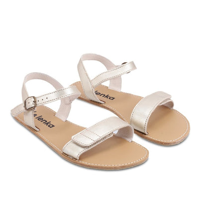 A photo of Gold Be Lenka Grace Sandals made with leather and tan rubber soles. The sandals have shiny gold straps and a single front foot strap with straps that go around the ankle and heel and have a small buckle. Both sandals are shown diagonally from the front right against a white background in this photo. #color_gold