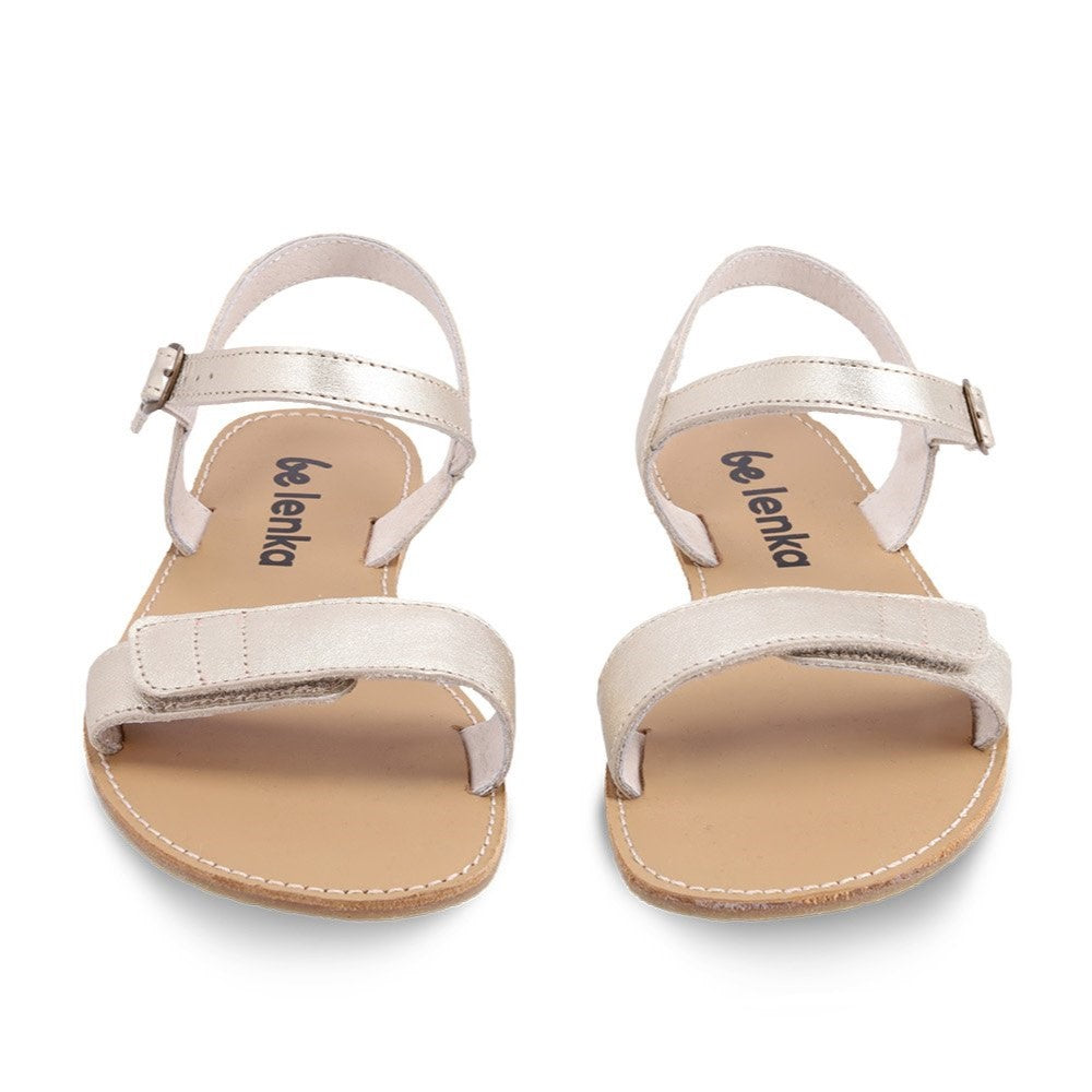 A photo of Gold Be Lenka Grace Sandals made with leather and tan rubber soles. The sandals have shiny gold straps and a single front foot strap with straps that go around the ankle and heel and have a small buckle. Both sandals are shown from the front against a white background in this photo. #color_gold