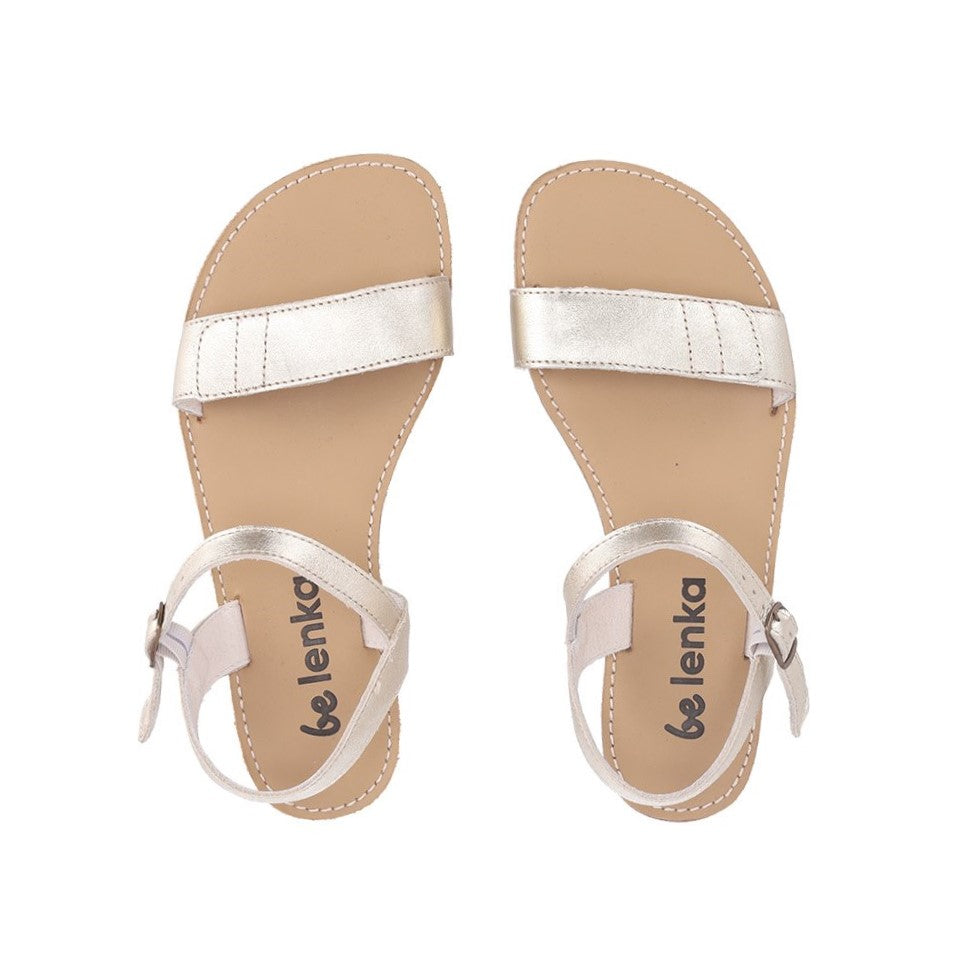 A photo of Gold Be Lenka Grace Sandals made with leather and tan rubber soles. The sandals have shiny gold straps and a single front foot strap with straps that go around the ankle and heel and have a small buckle. Both sandals are shown diagonally from the top down against a white background in this photo. #color_gold