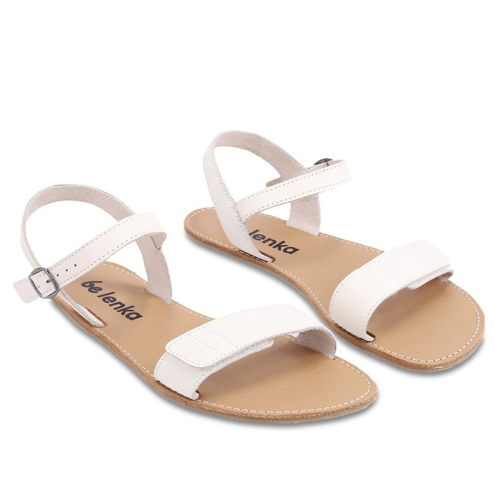 A photo of Ivory Be Lenka Grace Sandals made with leather and tan rubber soles. The sandals have shiny gold straps and a single front foot strap with straps that go around the ankle and heel and have a small buckle. Both sandals are shown diagonally from the front right against a white background in this photo. #color_ivory