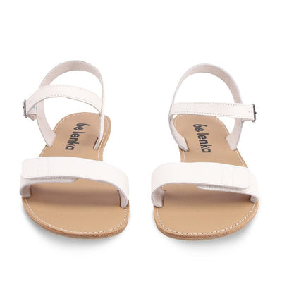 A photo of Ivory Be Lenka Grace Sandals made with leather and tan rubber soles. The sandals have shiny gold straps and a single front foot strap with straps that go around the ankle and heel and have a small buckle. Both sandals are shown from the front against a white background in this photo. #color_ivory