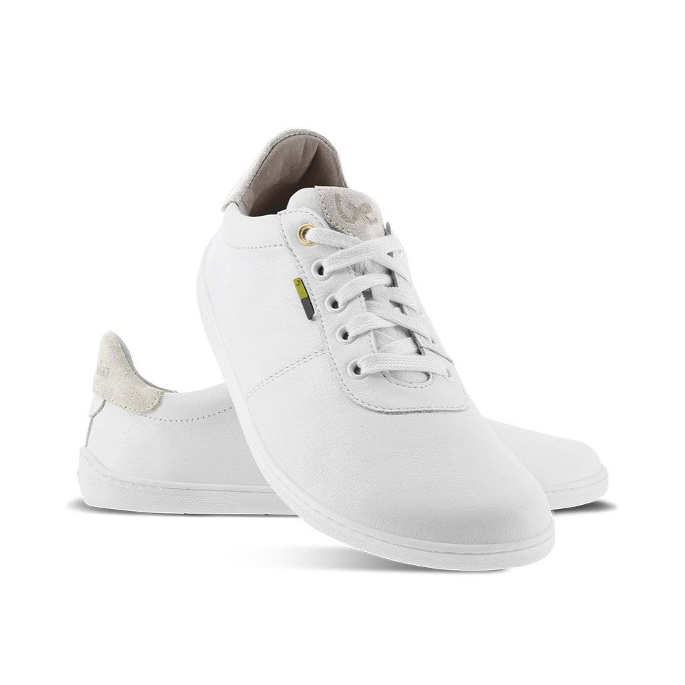 A photo of Be Lenka Royale sneakers made with a leather upper and a rubber sole. The sneakers are a white color and the area around the heel is beige, they have small yellow and blue tag on the side. Both shoes are shown, the left shoe is behind the right. The right shoes heel is leaning up against the left shoe showing the right shoe from the front facing down against a white background. #color_white-beige