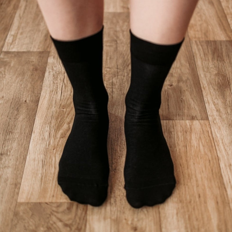 A photo of Be Lenka crew cut socks in black. Boths socks are show here on feet from the top down atop a brown wooden floor. #color_black