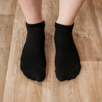 A photo of Be Lenka low cut socks in black. Boths socks are show here on feet from the top down atop a brown wooden floor. #color_black