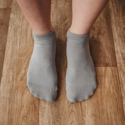 A photo of Be Lenka low cut socks in grey. Boths socks are show here on feet from the top down atop a brown wooden floor. #color_grey