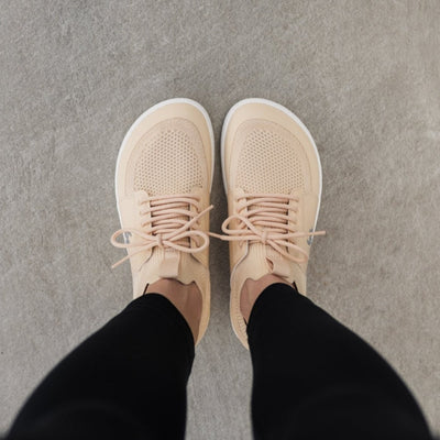 Photo 1 - A photo of Beige Cream Be Lenka Swift knit sneakers with white soles, and a harder material guarding the parimeter of the sole. Shoes are sock-like slip-ons with pull tabs at the tongue and heel with added laces. Right sneaker is shown facing right here against a white background. Photo 2 - Both shoes are shown from above on a person standing on a cement floor. #color_beige-cream