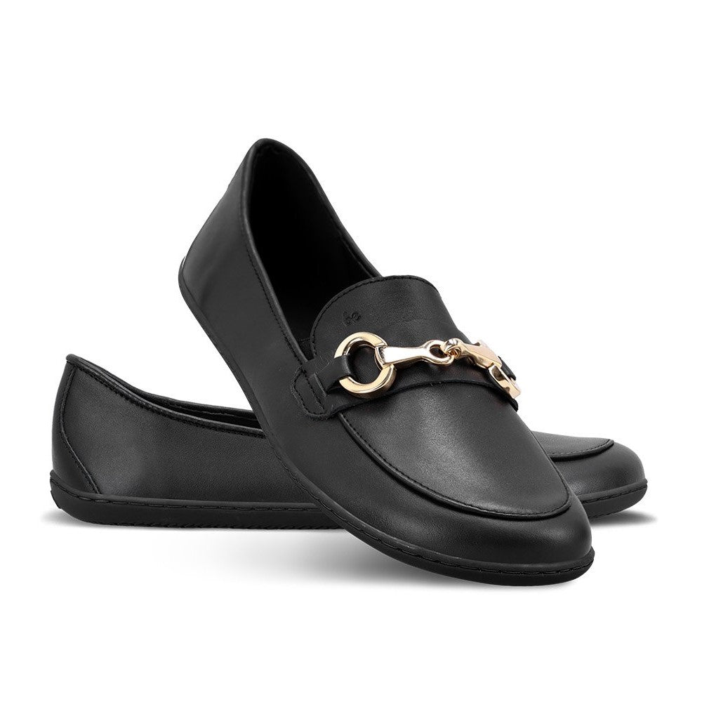 A photo of Black Be Lenka Viva leather loafers. A gold buckle detail graces the vamp. TR soles are stitched on for longevity. Right shoe is shown here facing right with the right shoe heel propped on top against a white background. #color_black