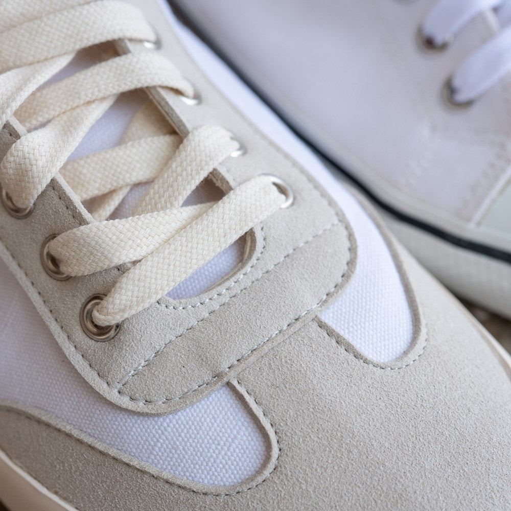 A photo of the Bohempia Felix vegan sneakers made from hemp canvas. The sneakers are white in color with a vegan suede tan toe cap and heel detail, with a tan sole and laces. The right shoe is shown from above with a focus on the laces and toe cap detail. #color_white-tan