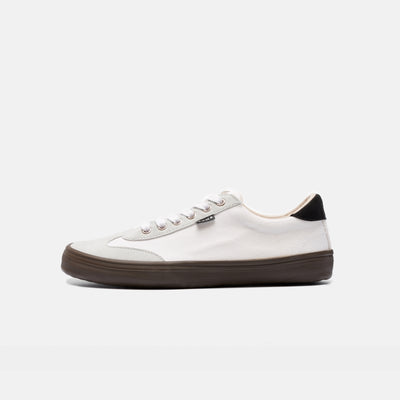 A photo of the Bohempia Felix vegan sneakers made from hemp canvas. The sneakers are white in color with a light grey vegan suede toe cap and a black heel detail, with a dark gum sole and white laces. The left shoe is shown from the left side on a white background. #color_white-dark-gum