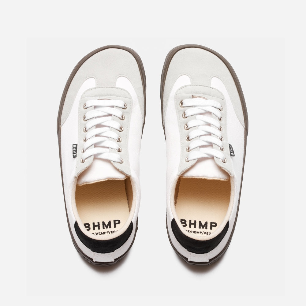 A photo of the Bohempia Felix vegan sneakers made from hemp canvas. The sneakers are white in color with a light grey vegan suede toe cap and a black heel detail, with a dark gum sole and white laces. Both shoes are shown from above on a white background. #color_white-dark-gum