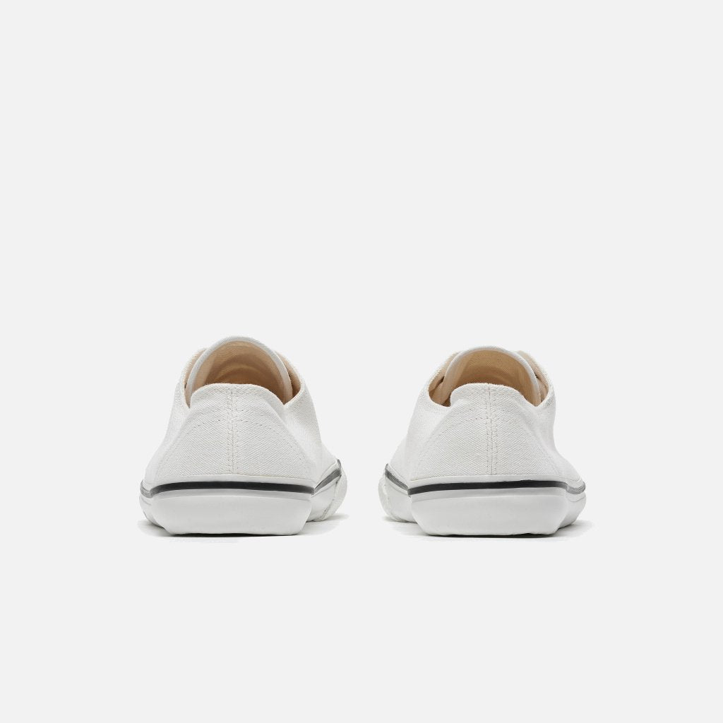 A photo of Bohempia Herlik canvas sneakers made from canvas and rubber soles. The sneakers are light white with a white toe cap and a black outline around the white rubber soles. Both sneakers are shown from the back against a white background. #color_white