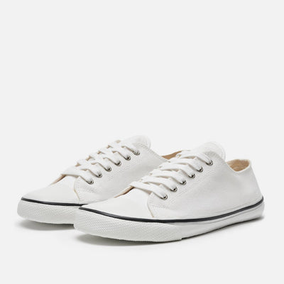A photo of Bohempia Herlik canvas sneakers made from canvas and rubber soles. The sneakers are white with a white toe cap and a black outline around the white rubber soles. Both sneakers are shown diagonally from the front left against a white background. #color_white