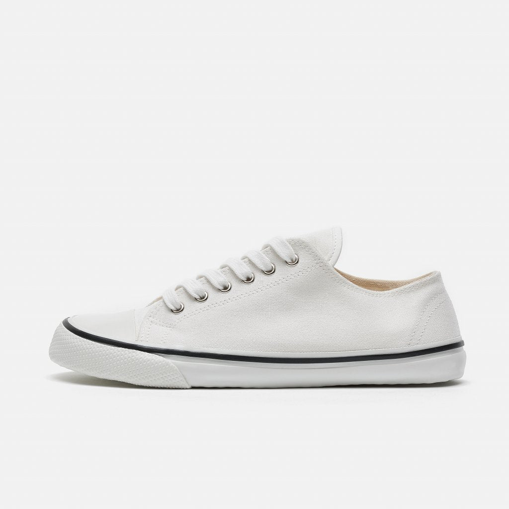 A photo of Bohempia Herlik canvas sneakers made from canvas and rubber soles. The sneakers are white with a white toe cap and a black outline around the white rubber soles. The left sneaker is shown from the left side against a white background. #color_white