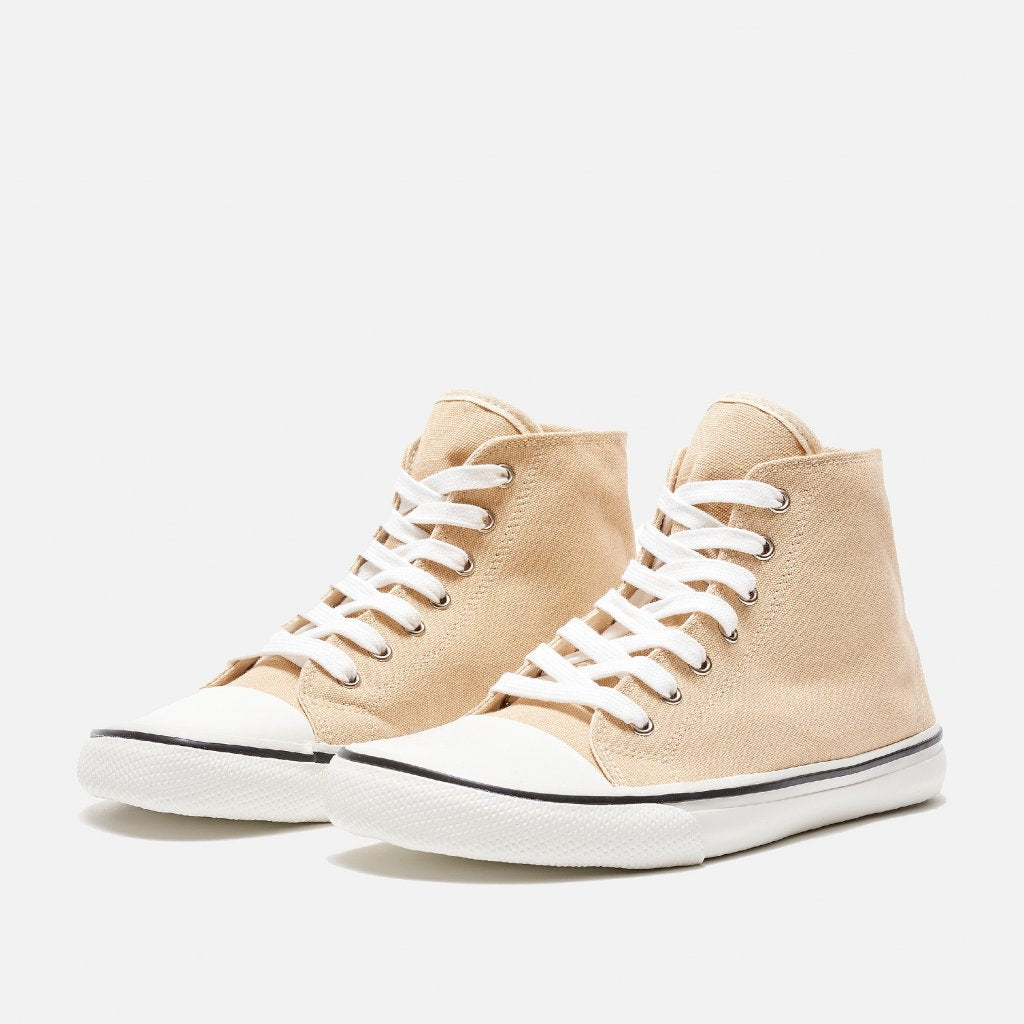 A photo of Bohempia Orik canvas high tops made from canvas and rubber soles. The sneakers are a tan color with a white toe cap and a black outline around the white rubber soles. Both sneakers are shown diagonally from the front left against a white background. #color_tan-white