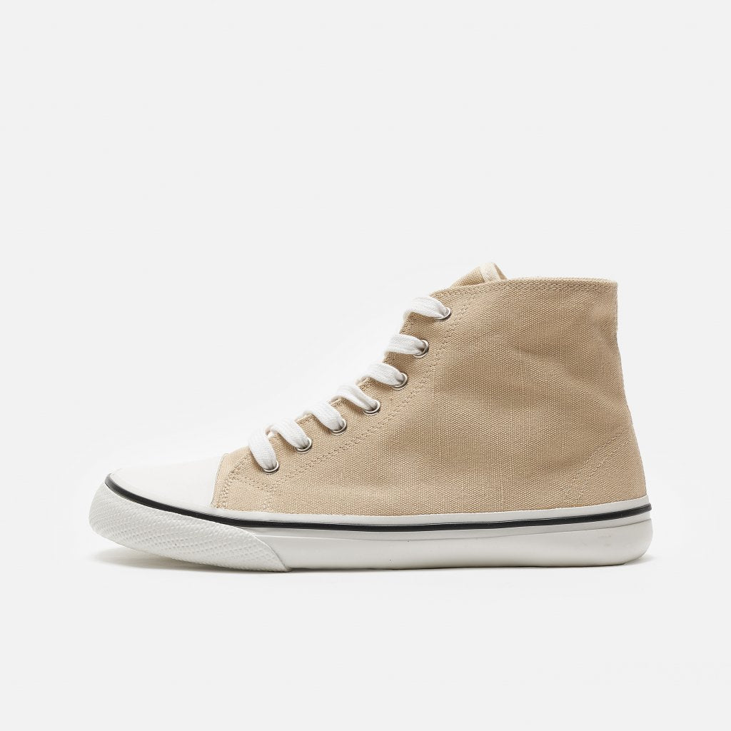 A photo of Bohempia Orik canvas high tops made from canvas and rubber soles. The sneakers are a tan color with a white toe cap and a black outline around the white rubber soles. The left sneaker is shown from the left side against a white background. #color_tan-white