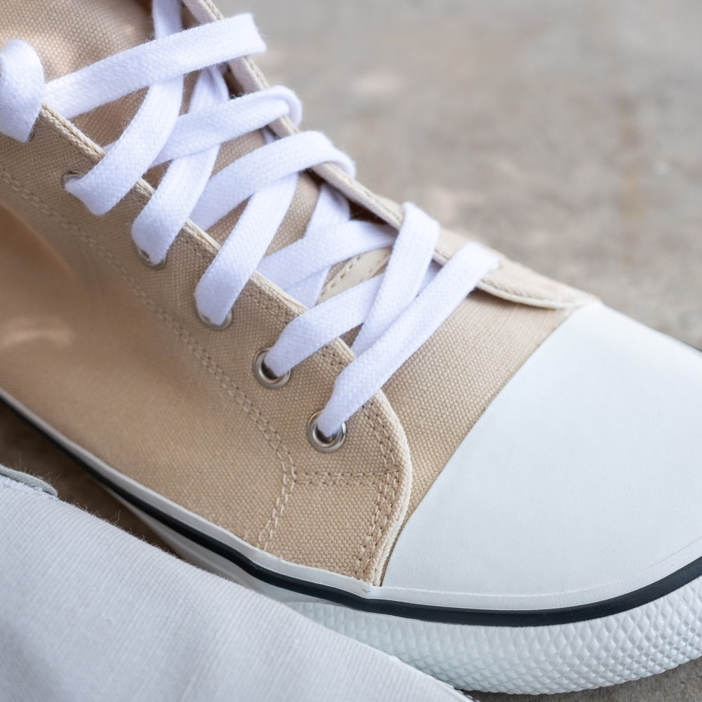 A photo of Bohempia Orik canvas high tops made from canvas and rubber soles. The sneakers are a black color with a white toe cap and a black outline around the rubber. The right sneaker is shown from above to show a close up of the laces and toe cap, with a cement floor background. #color_black-white