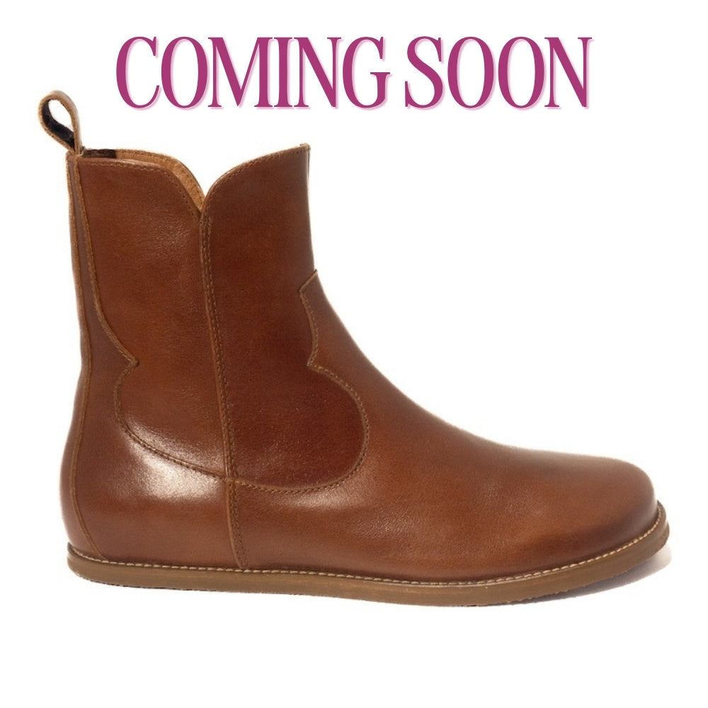 Smooth brown leather western Faye boots By Anya with a western shape on both sides of the ankles, a zipper, tan rubber soles, a welt stitching design around the top of the sole, and a pull tab at the top back of the opening. Right boot is shown facing right against a white background. #color_cognac