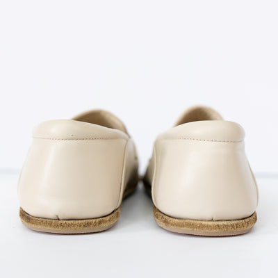 A photo of Dalia Leather loafers Designed by Anya with a leather upper and tan rubber soles. The loafers are a beige smooth leather upper and have a matching leather strap across the top of the foot for design. Both loafers are shown together from the behind against a white background. #color_beige