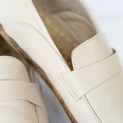 A photo of Dalia Leather loafers Designed by Anya with a leather upper and tan rubber soles. The loafers are a beige smooth leather upper and have a matching leather strap across the top of the foot for design. The left loafer is shown with a close up of the leather strap detail. #color_beige