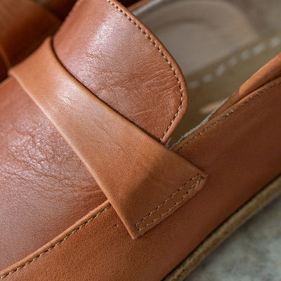 A photo of Dalia Leather loafers Designed by Anya with a leather upper and tan rubber soles. The loafers are a brown smooth leather upper and have a matching leather strap across the top of the foot for design. The left loafer is shown with a close up of the leather strap detail. #color_brown 