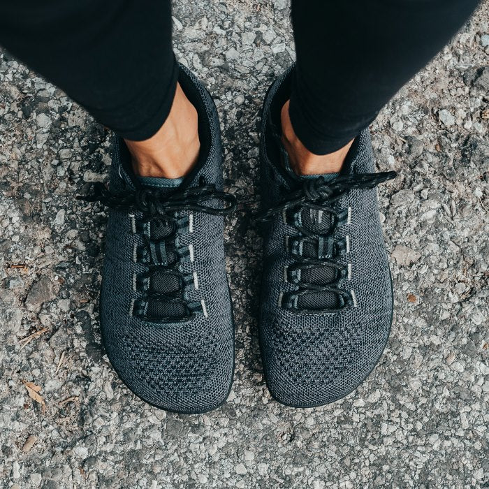 A photo of Freet Pace sneakers in charcoal. Sneakers are completely knit and have a detatched tongue. Laces are black and loop through fabric tabs attached to the shoe and a tab on the tongue. Both shoes are shown here from the top down on pavement. #color_charcoal