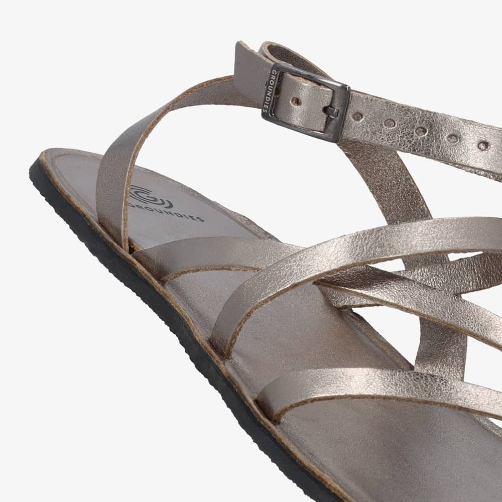 A photo of dark gold metallic leather Groundies Florence Sandals. Two leather straps start at the ball of the big toe with one ending at the ball of the little toe and the other midfoot. Another strap goes from one side of the heel over the top of the foot to the other side with one final strap wrapping around the ankle and closing with a buckle. The right shoe is shown from the right side against a white background with a focus on the buckle detail. #color_dark-gold