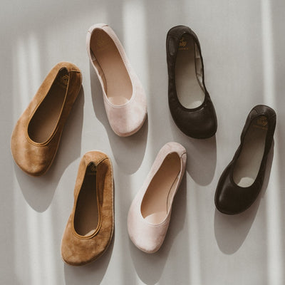 A photo of Groundies Lily Classic flats with a leather upper and tan rubber true sense soles. The flats are a perforated leather in a cognac color with trim around the tops. The interior of the flats is a light beige color. A pair of these flats are on the left, a pair of light pink Lily Soft flats are in the middle, and a pair of black Lily Classic flats on are the right, all shown from above on a white background. #color_cognac