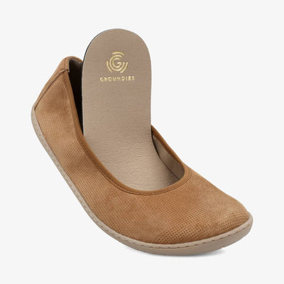A photo of Groundies Lily Classic flats with a leather upper and tan rubber true sense soles. The flats are a perforated leather in a cognac color with trim around the tops. The interior of the flats is a light beige color. The right shoe is shown from the front with the heel of the removeable insole out of the shoe, on a white background. #color_cognac